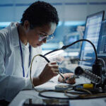 Modern Electronics Research, Development Facility: Black Female Engineer Does Computer Motherboard Soldering. Scientists Design PCB, Silicon Microchips, Semiconductors. Medium Close-up Shot