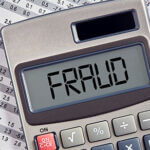 Calculator spelling out the word "FRAUD" over financial papers