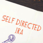 Paper reading "Self Directed IRA" in red with hand drawn magnified glass