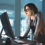 Woman standing at a desk looking at large computer monitor