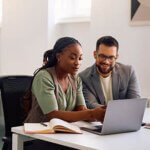 Couple sitting side by side looking at something on a laptop