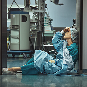 Woman surgeon looking sad and fatigued on the floor of a hospital room
