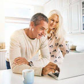 Older couple sitting at a counter in a kitchen looking at a laptop